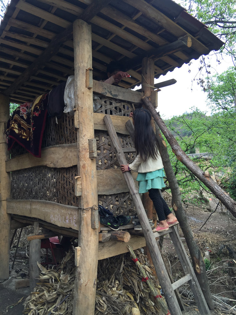 小女孩爬梯子給住在村中包谷垛子高處的吸毒艾滋患者遞火機。(作者供圖)