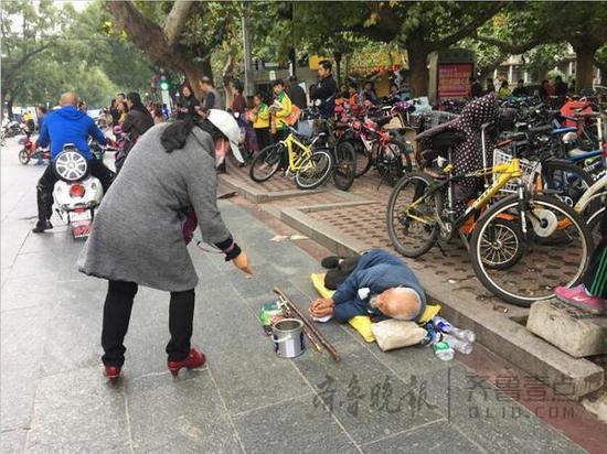 泰安一中北臨，一名乞丐躺在地上，來往市民不時(shí)地給他施捨一些零錢。